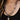 Close up of a woman wearing multiple necklaces, including a diamond chain with a pink heart charm, a ball chain with a yellow/pink seashell charm, a pearl necklace, and a gold chain with a key pendant and a diamond charm